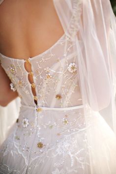 the back of a woman's wedding dress with flowers and beads on her shoulders