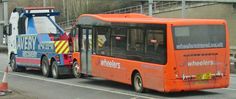 an orange bus driving down the road next to a blue truck with a crane on it's back