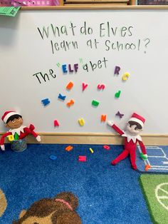 two elfs are sitting on the floor in front of a whiteboard with letters