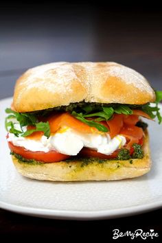 a sandwich with tomatoes, mozzarella and lettuce on a white plate