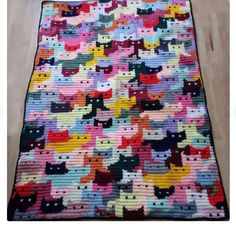 a multicolored crocheted rug with cats on it, sitting on a wooden floor