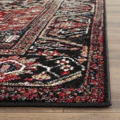 a black and red area rug with an ornate design on the center, in front of a wooden floor