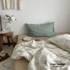 an unmade bed with white sheets and pillows on top of it, next to a small wooden table