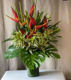 a vase filled with red and green flowers on top of a white table next to a curtain