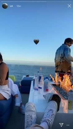 two people sitting at a table on top of a boat with an open fire pit