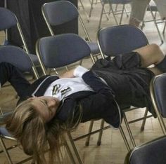 a woman laying on top of a chair in a room filled with chairs and people