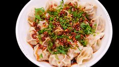 a white plate topped with dumplings covered in sauce and green garnishes