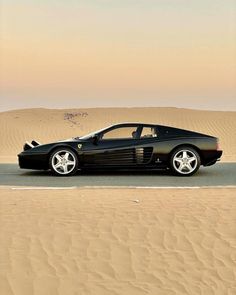 a black sports car in the desert with sand dunes behind it and a sky background