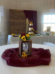 a table topped with a vase filled with sunflowers and a cake on top of it