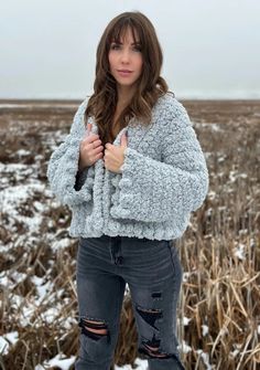 a woman standing in the middle of a field wearing ripped jeans and a fuzzy sweater