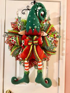 a christmas wreath hanging on the front door with elf legs and stockings attached to it