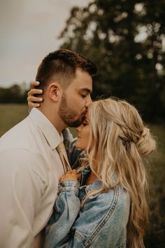 a man and woman kissing each other in the middle of a field with trees behind them