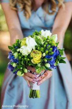 a woman in a blue dress holding a bouquet of white and yellow flowers on her wedding day