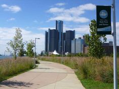 a sidewalk with a sign on it next to the water and tall buildings in the background