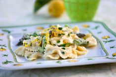 a white plate topped with pasta and asparagus on top of a table next to a green cup