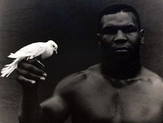 a man holding a white bird in his right hand and looking at the camera while standing next to him