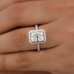 a woman's hand holding an engagement ring with a square shaped diamond in the center