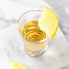 a small glass filled with liquid and sliced lemons on a white marble counter top