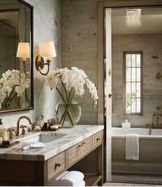 a bathroom with marble counter tops and white flowers in a glass vase on the sink