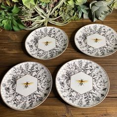 four black and white plates with honeybees on them sitting on a wooden table