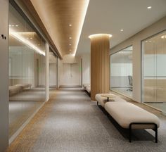 a long hallway with benches and glass doors leading to the other rooms in an office building