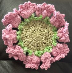 a crocheted pink and green flower sitting on top of a black couch