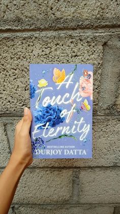 a person holding up a book in front of a brick wall with butterflies on it