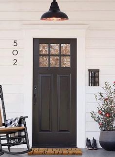 a rocking chair on the front porch of a white house with black door and numbers