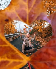 a woman sitting on the ground in front of a heart - shaped frame with leaves