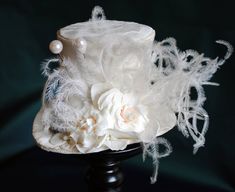 A Mad Hatter fascinator hat with a bridal twist! The hat is covered with beautiful textured ivory brocade and embellished with ivory satin ribbon around the crown. Trimmed with pearl hats pins, ivory roses and hydrangea blossoms,ivory feather spray, the signature 10/6 Mad Hatter card and of course a tiny silver tea-pot! Cause around here it's always tea-time! Both hat pins have push-in clasps to avoid accidents! Veil may be added at an extra cost. This mini top hat is fully lined with satin and White High Crown Adjustable Mini Hat, White Adjustable High Crown Mini Hat, White High Crown Top Hat For Church, White High Crown Mini Hats For Church, Vintage White Hat With High Crown, White Vintage Top Hat With Curved Brim, Vintage White High Crown Hat, Vintage White Mini Hat With Short Brim, White Fitted Hats For Vintage Events