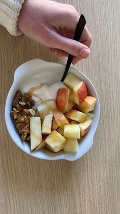 a person is holding a spoon over a bowl of fruit