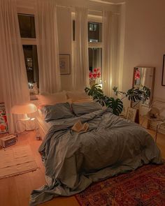 a bed with blue sheets and pillows in a bedroom next to a large window filled with potted plants