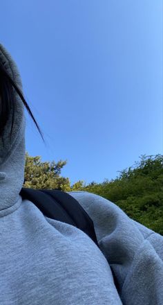 a person wearing a hoodie and holding a cell phone up to their ear with trees in the background