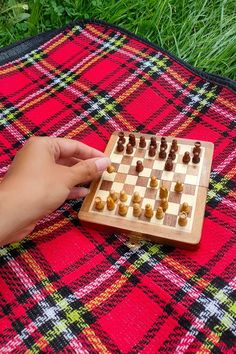 a person is playing chess on a blanket in the grass with their hand over the board