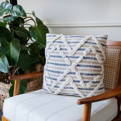 a white and blue pillow sitting on top of a chair next to a potted plant