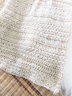 a white knitted blanket sitting on top of a wicker floor next to a pillow