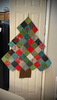 a quilted christmas tree hanging on the front door with a refrigerator in the background