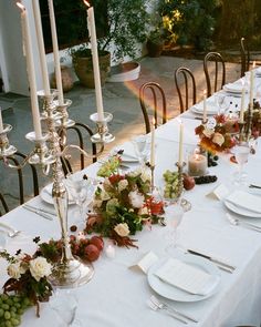 a long table is set with white plates and silverware, candles, and flowers