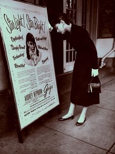 a woman standing next to a poster on the sidewalk