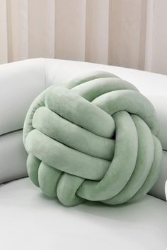 a green knot pillow sitting on top of a white couch next to a cup and saucer