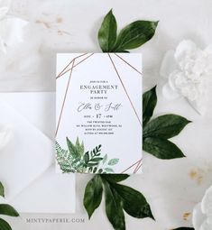 the wedding stationery is surrounded by greenery and white flowers on top of an envelope