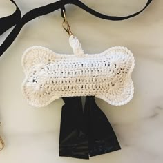 a white crocheted dog bone shaped purse on a black leash next to a pair of scissors