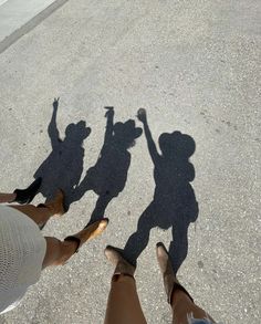 three people standing in the street with their shadows on the ground and one person holding her hand up