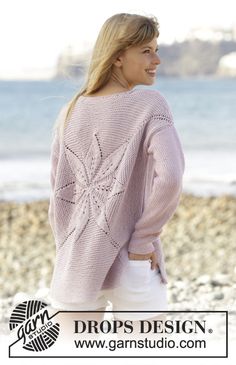 a woman standing on the beach with her back to the camera, wearing a pink sweater and white pants