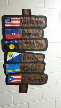 a welcome sign hanging on the side of a wall with flags and words written in different languages