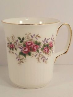 a white cup with pink flowers painted on the side and gold trim around the rim