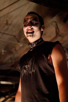 a man in black shirt with blood on his face and mouth, standing under a ceiling