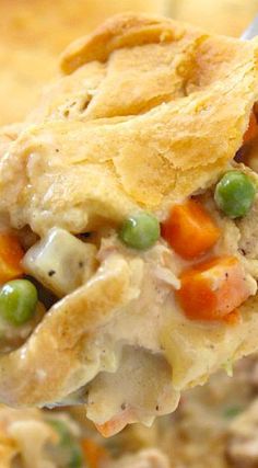 a spoonful of chicken pot pie with peas and carrots on it, in a casserole dish