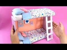 someone is holding up a doll house made out of cardboard and fabric materials that looks like a bunk bed