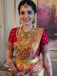 a woman in a red and gold sari with jewelry on her neck, smiling at the camera